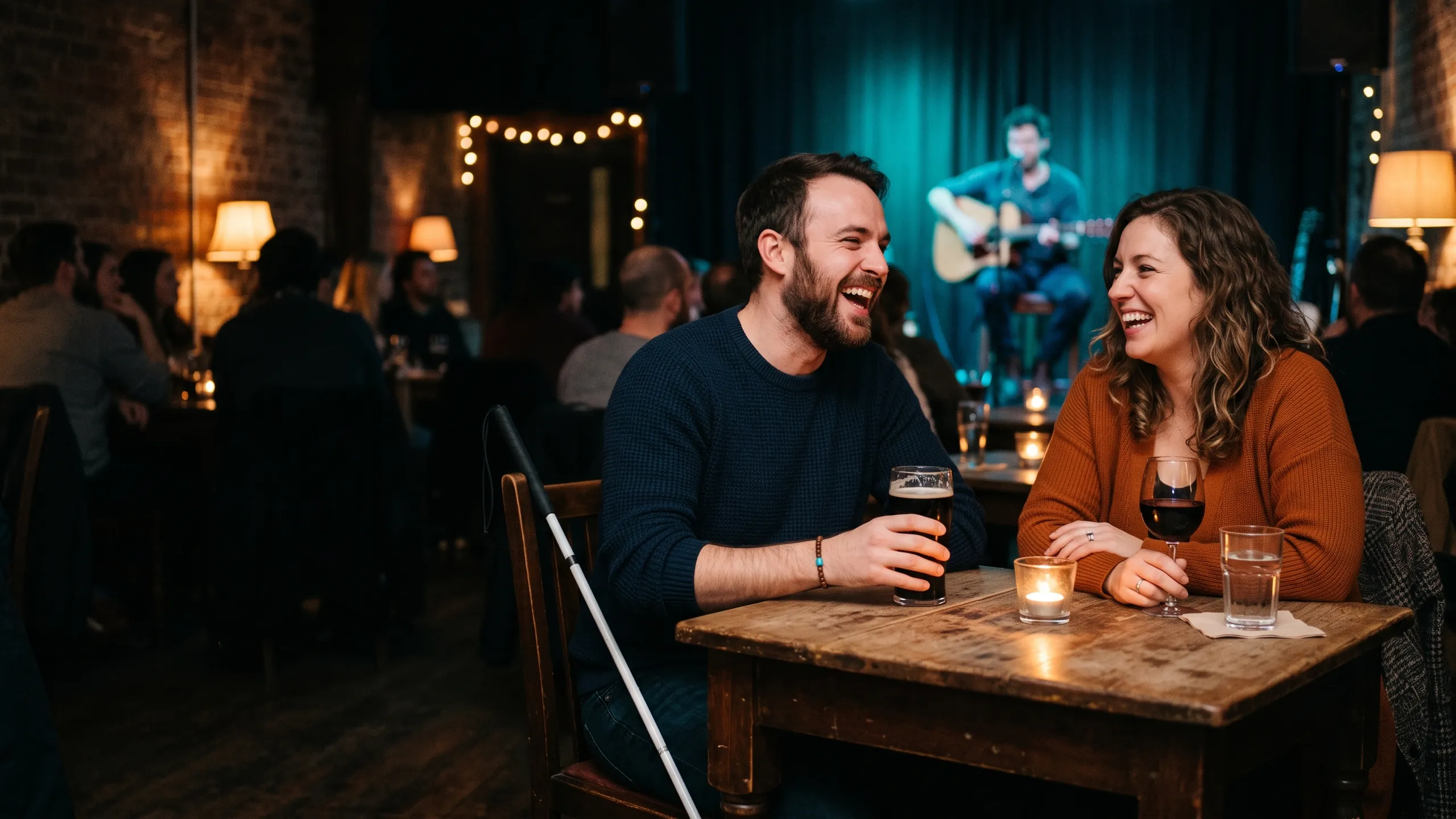 A couple laughing at a candlelit table in a small live-music venue, a white cane resting beside the seat